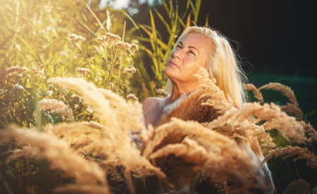 A Radiant Woman Stands Gracefully Among Golden Grasses at Sunset, Capturing Beauty and Calmnessの写真素材
