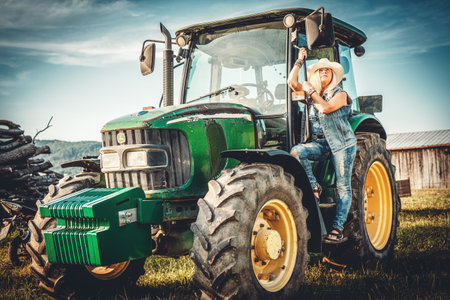 A woman in a cowboy hat poses on a tractor.の写真素材