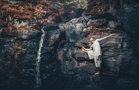 A woman practices yoga on the rocks near a waterfall.の写真素材