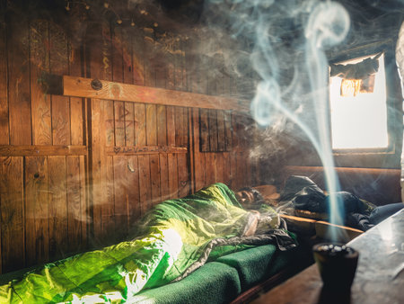 Mysterious light streaming through an old window in a mountain hut at sunrise, the light shines on a woman in a green sleeping bag, the scene is shrouded in smoke from incense.の写真素材