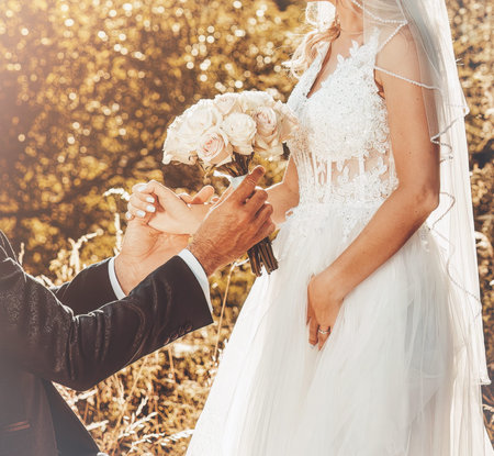 Groom and bride holding a beautiful floral bouquet in beautiful summer nature