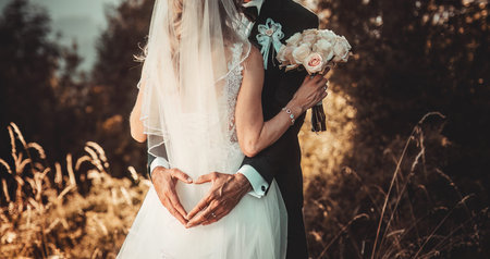 Groom and bride holding a beautiful floral bouquet in beautiful summer nature