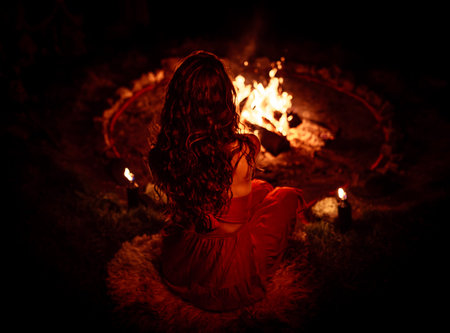 Woman sitting by the fire, back view. Night Cacao Ceremony.