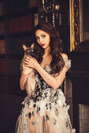 Gorgeous glamorous woman in dress standing with cat. Brunette beautiful stunning girl looking at you. Vogue style portraitの写真素材