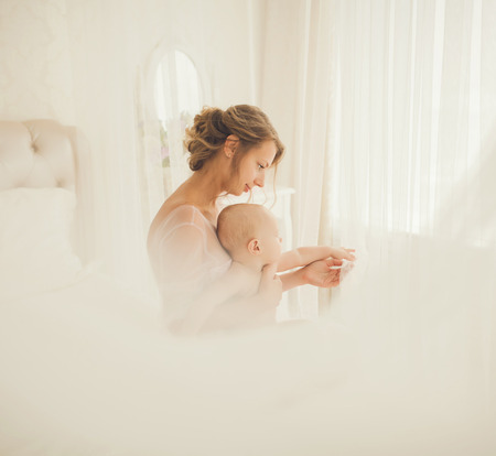 Happy mother and baby sitting on the bed in the roomの写真素材