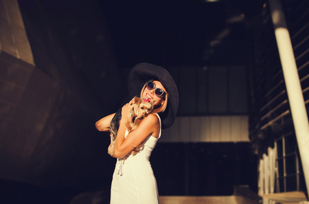 Portrait of a happy blonde in elegant hat with dog. Beauty, fashion concept.の写真素材