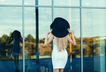 Luxury travel vacation woman standing back near hotel. Elegant young lady wearing sexy dress and big hat on holidays.の写真素材