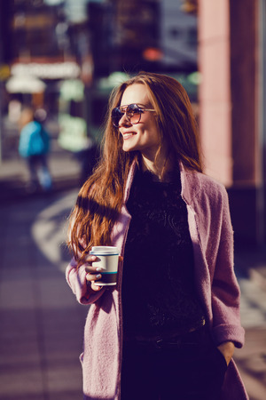 Beautiful elegant lady in a coat and sunglasses drinking coffee and laughingの写真素材