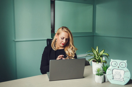young business woman with phone sitting in office with laptopの写真素材