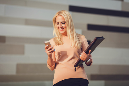 Business woman portrait outdoors with phone and folder outdoorsの写真素材