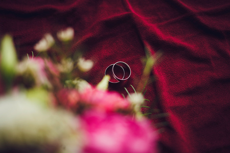Beautiful wedding rings lie on a red textileの写真素材