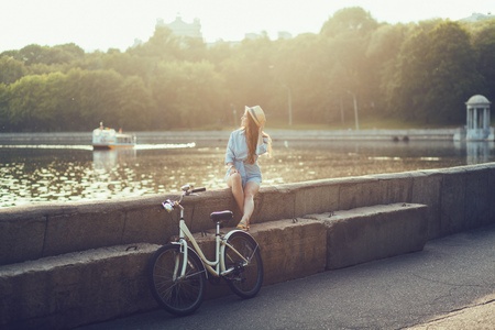 Charming woman in dress walking bicycle enjoying sunset. Girl with sun hat relaxingの写真素材