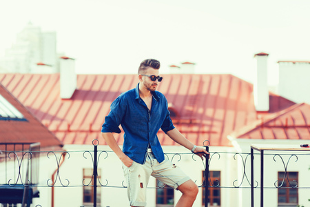 Young handsome man in summer clothes is posing on roof of the cityの写真素材