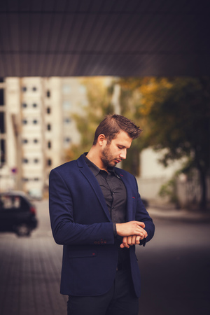 I will be in time. Handsome man in formalwear looking at his watch while standing at the streetの写真素材