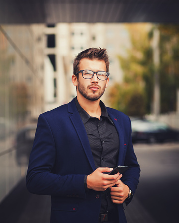 Young urban businessman professional on smartphone in street using app texting sms message on smartphone wearing jacketの写真素材