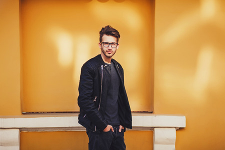 Fashionable man in leather jacket and glasses posing on background of colored wallの写真素材