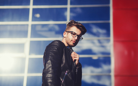 Gorgeous and stylish. Handsome young man in glasses and jacket posing against blue backgroundの写真素材