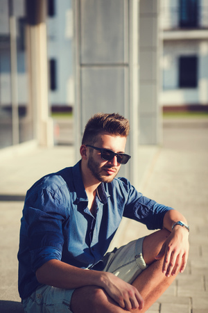 Handsome man in a shirt and sunglasses is sitting in the cityの写真素材
