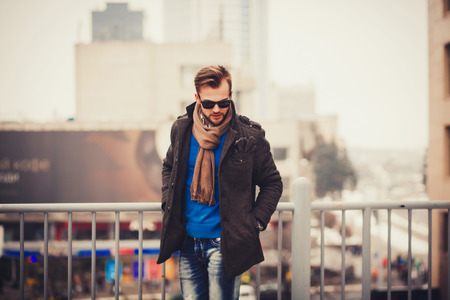 Trendy handsome young man in autumn fashion standing in urban environmentの写真素材