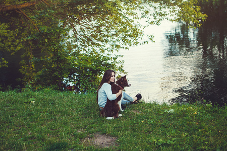 Woman and her dog sitting outdoor. Girl loving and hugging tightly her dog and watching on riverの写真素材