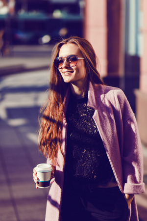 Summer sunny lifestyle fashion portrait of young stylish woman walking on street, wearing cute trendy outfit,drinking hot latteの写真素材
