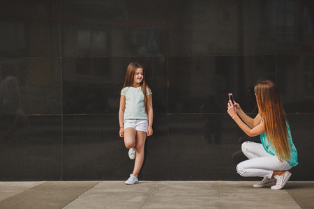 Happy mother taking portrait child on smartphone in city, family wearing a t-shirts and white shortsの写真素材