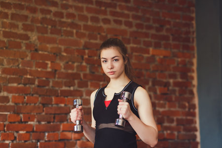 Active sportive athletic woman with dumbbells pumping up muscles in gymの写真素材