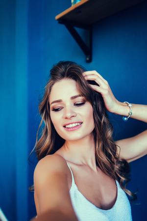 Pretty brunette woman in white dress making selfie at the camera over blue backgroundの写真素材