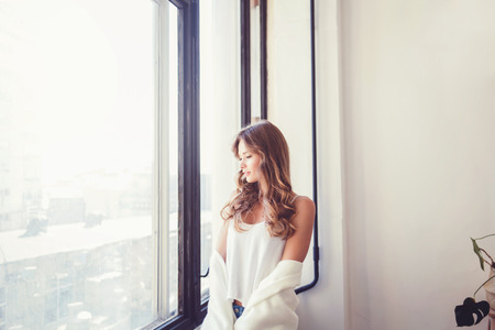Beautiful woman in t-shirt near window in the morningの写真素材
