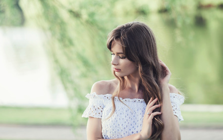 Portrait of a beautiful girl in a white dress in a field at sunset in summer. copy spaceの写真素材