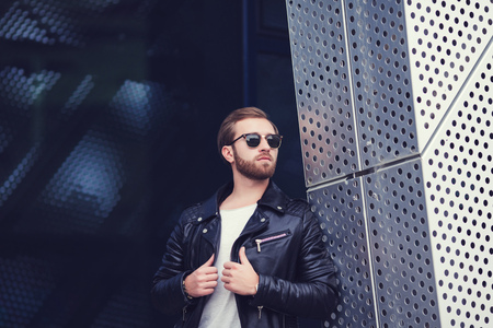 Portrait of brutal young man wearing black jacket and posing over urban background.  Hipster style. Copy-space.の写真素材