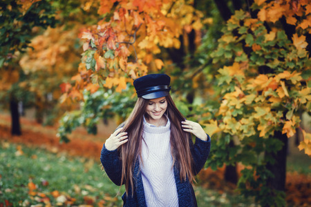 portrait of a beautiful girl in sweater and black hat standing near colorful autumn leaves. Art work of romantic woman .の写真素材