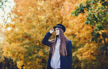 Young autumn woman in coat and black hat on leaves backgroundの写真素材