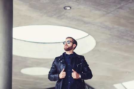 stylish man in a leather jacket and glasses posing on a gray backgroundの写真素材