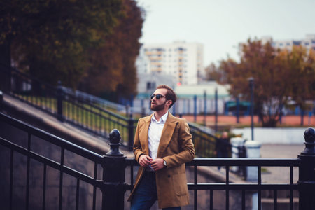 Handsome confident male model in elegant coat and shirt posing in autumn park