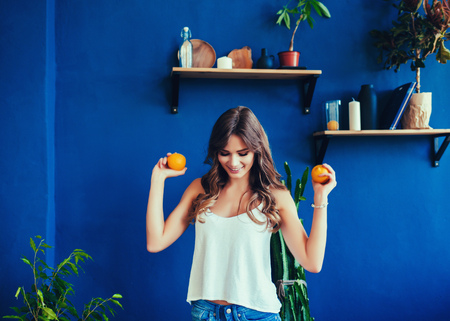 Young woman on vibrant blue background holds orange in her hands. Concept of healthy food and lifestyleの写真素材