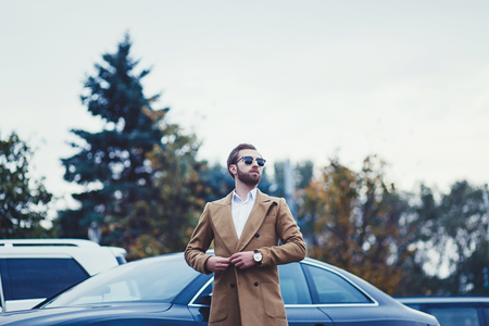 young rich man in a coat against the background of the carの写真素材