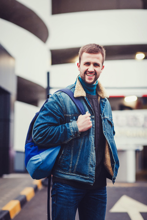 Stylish guy standing street in a denim jacket and backpackの写真素材
