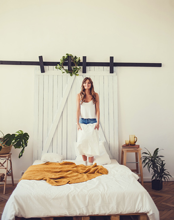 Happy young beautiful woman jumping on the bed at home with pillow.の写真素材