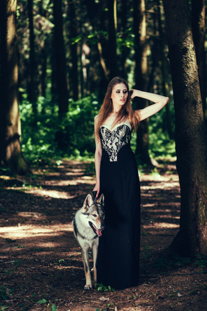 full-length portrait of a woman in a black dress with a dog in forestの写真素材