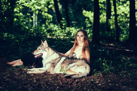 Attractive young woman with wolf dog in dark forestの写真素材