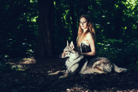 Glamorous girl sitting with dog wolf in forestの写真素材
