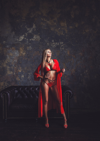sexy blonde model in red lingerie posing near leather sofaの写真素材