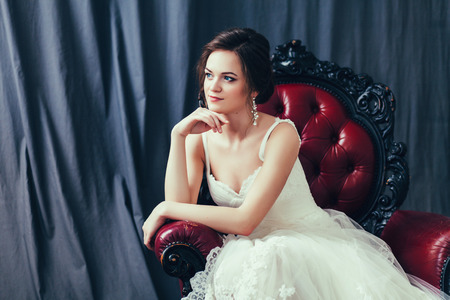 Beautiful bride in white wedding dress with bridal bouquet at armchairの写真素材
