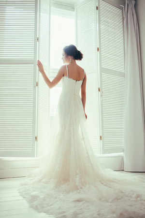 Luxury bride in dress near window on a light background.の写真素材