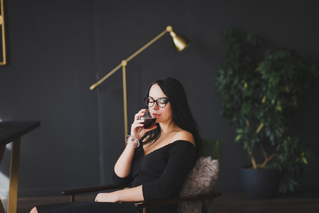 Beautiful brunette woman in black dress drinking red wineの写真素材