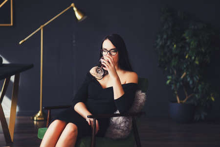 glamorous lady with glasses and black dress drinks red wineの写真素材