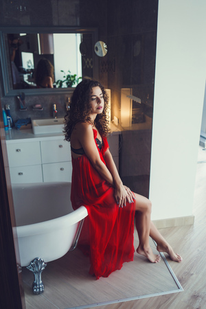 Curly woman sitting in bathroom wearing red dressの写真素材