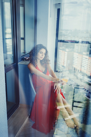 Beautiful and sexy brunette woman in red dress on balconyの写真素材