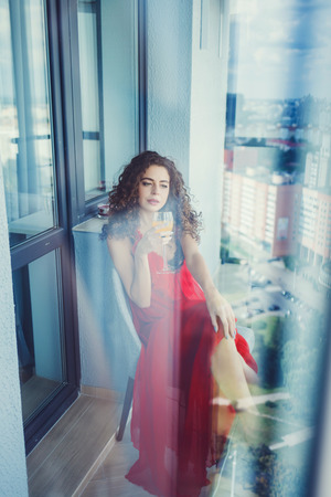 portrait of a curly woman in a red dress with a glass of juiceの写真素材